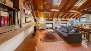 A cozy living room with a fireplace, bookshelves, a sofa, and a dining area. - 'The Traveler’s Attic' Apartment with Mountain View, Private Terrace and Wi-Fi (Pont Saint Martin)