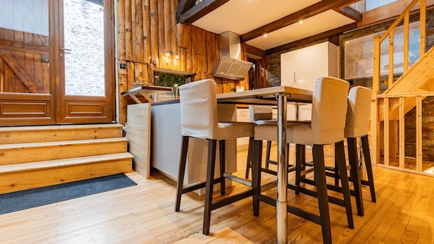 A wooden interior with a kitchen, bar stools, and a staircase.
