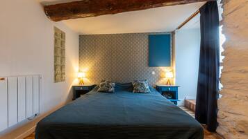 Un dormitorio con una cama grande, dos mesitas de noche con lámparas, un radiador y una pared de piedra.