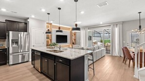 Une cuisine moderne avec des meubles de couleur sombre, des appareils électroménagers en acier inoxydable et des luminaires suspendus.