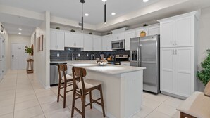 Una cocina moderna con armarios blancos, una isla central con taburetes y electrodomésticos de acero inoxidable, además de un salpicadero de azulejos.