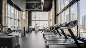 Ein Fitnessstudio mit Laufbändern, Fahrrädern und Gewichten, große Fenster mit Blick auf die Stadt.