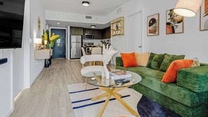 Ein modernes Wohnzimmer mit einem grünen Sofa, einem Glastisch und einem Essbereich im Hintergrund.