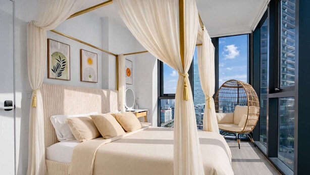 Ein modernes Schlafzimmer mit einem Himmelbett, Blick auf die Stadt und einem Korbstuhl.