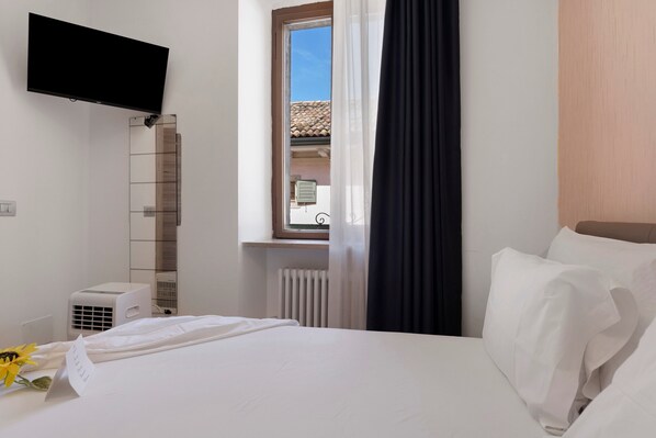 A hotel room with a bed, a flat-screen TV mounted on the wall, a window with a view of the outside, and a radiator.