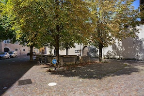 A cobblestone street with a tree-lined sidewalk, a directional sign, and parked cars.