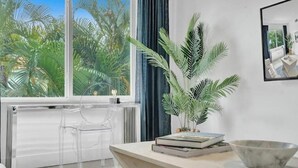 A modern room with a large window, a clear view of palm trees outside, a marble bowl, and a clear chair.