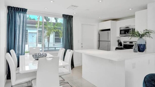 A modern kitchen with white cabinetry, a central island, and a dining area with a white table and chairs.