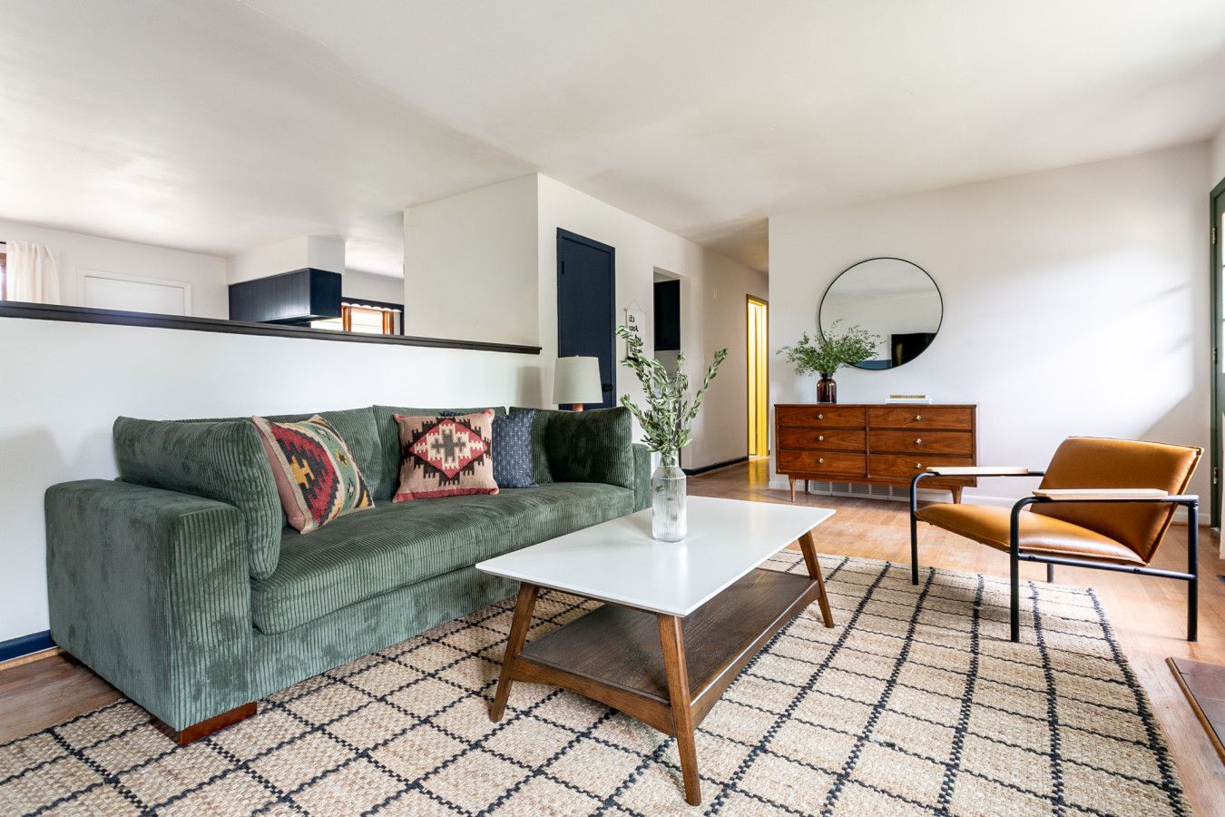 A modern living room with a green sofa, a white coffee table, and a brown armchair.