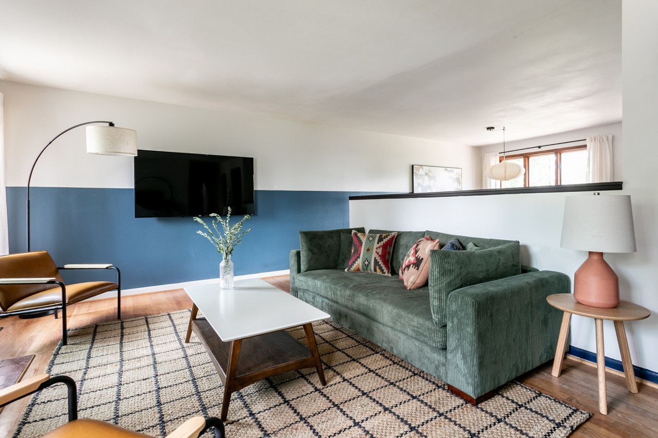 Ein Wohnzimmer mit einem grünen Sofa, einem weißen Couchtisch, einem braunen Ledersessel, einer Stehlampe und einem kleinen Beistelltisch mit einer Lampe.