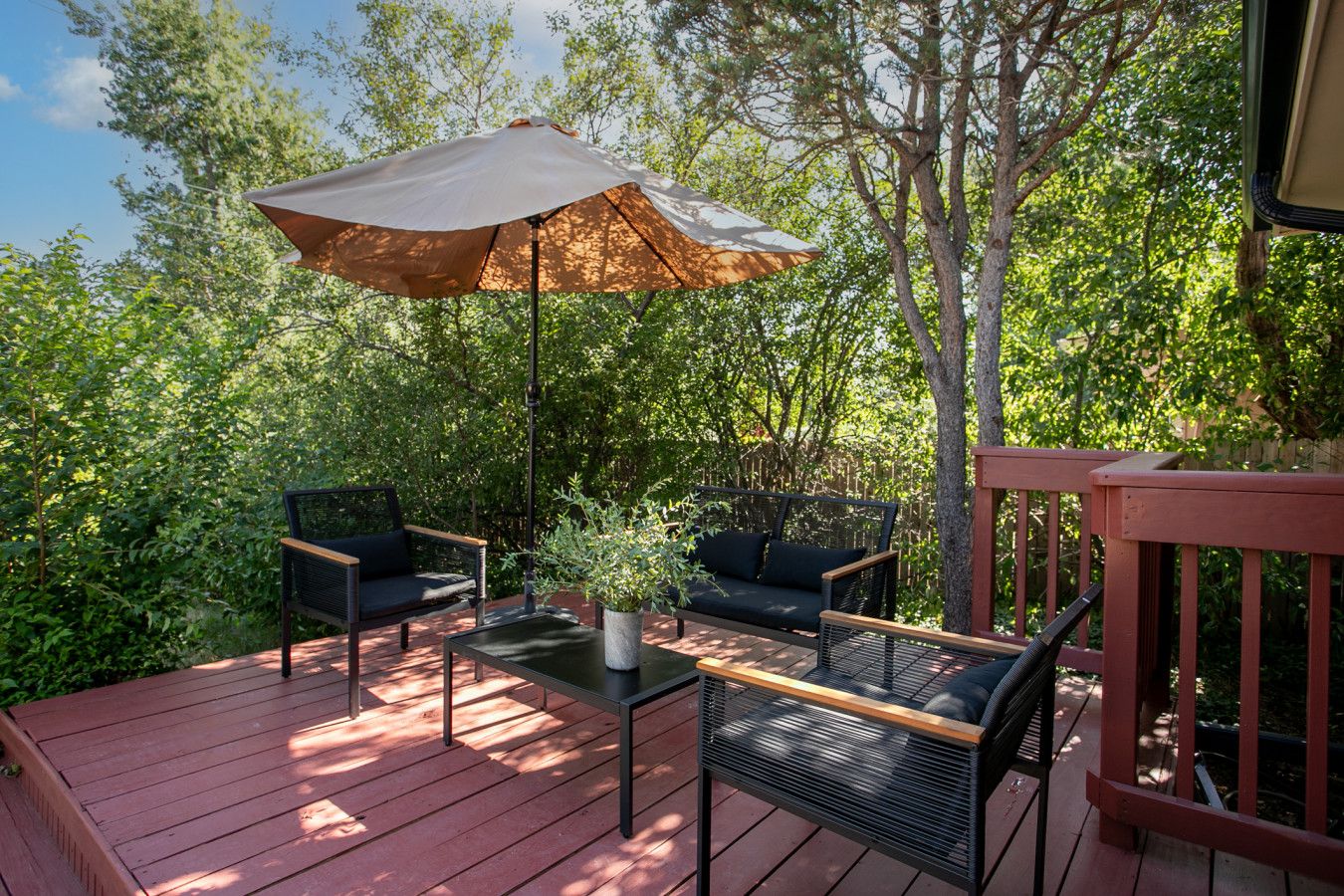 Une terrasse en bois avec deux canapés en osier noir, une petite table et un parasol.