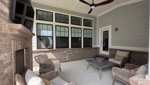 Un patio techado con mobiliario de mimbre, chimenea y ventanas amplias.