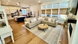 Un salón espacioso con un amplio sofá seccional en forma de L, una mesa de centro y un comedor, con una cocina al fondo.