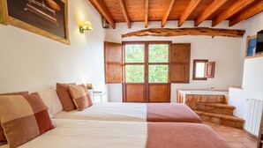 Ein Schlafzimmer mit zwei Betten, Holzbalken, einem Fenster mit Blick und einem kleinen Badezimmer mit Waschbecken.