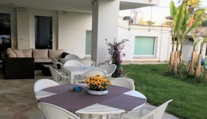En udendørs terrasse med spisebord, stole og blomsterarrangement.
