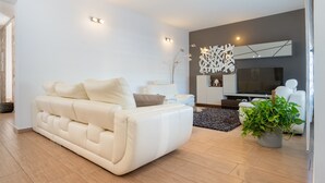 Un salon moderne avec un canapé, un téléviseur, des œuvres d’art décoratives au mur et une plante en pot.