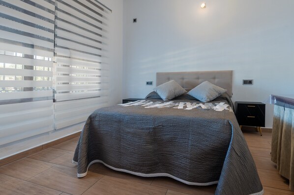 A bedroom with a bed, a nightstand, a wall-mounted light, and a window with blinds.