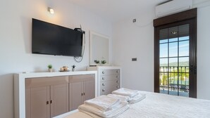 Une chambre à coucher comprenant un lit, un téléviseur fixé au mur, une commode et une porte donnant sur un balcon extérieur.