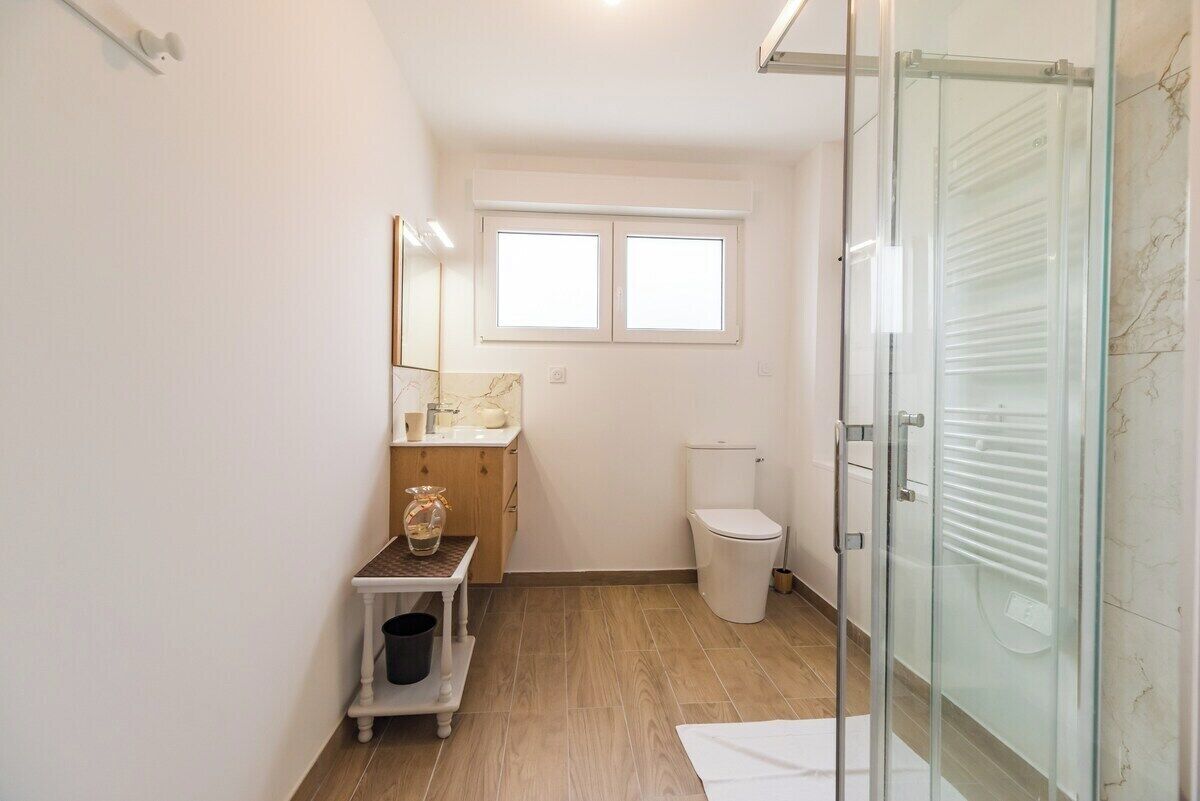 Une salle de bain moderne avec une douche à l’italienne en verre, des toilettes et un petit meuble-lavabo avec un miroir.