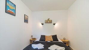 Ein ordentlich bezogenes Bett mit zwei Handtüchern, einer Wanduhr und einem gerahmten Bild.