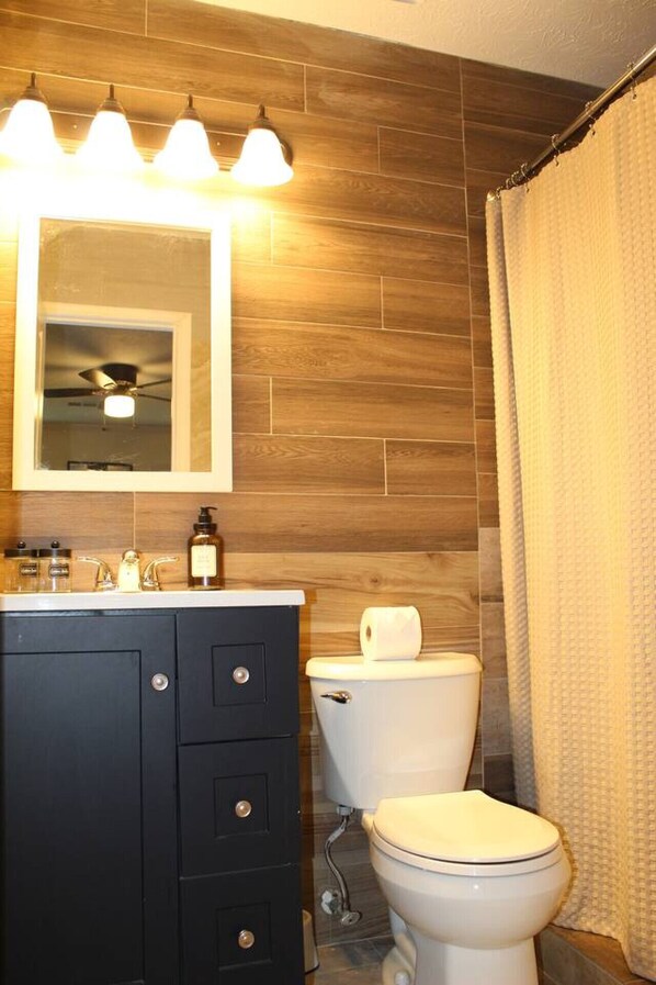 A bathroom with a wooden wall, a black vanity with drawers, a mirror, and a toilet.