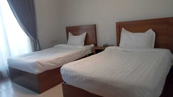 Une chambre d’hôtel avec deux lits simples, des têtes de lit en bois, du linge de lit blanc et une table de chevet avec une lampe.