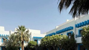 A pool area with lounge chairs, a palm tree, and a building with blue accents. - Golden Square Resort (Riyadh)