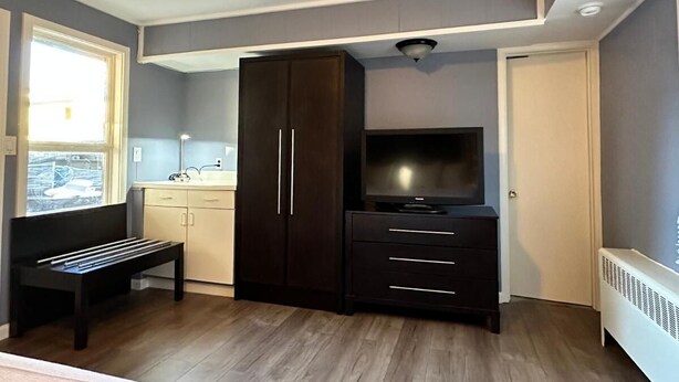 Une pièce avec une armoire en bois sombre, un téléviseur, un banc et une fenêtre donnant sur un bâtiment à l’extérieur.