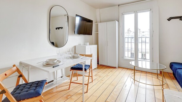 Une pièce moderne et bien éclairée, avec une table à manger, des chaises, un téléviseur et une grande fenêtre.