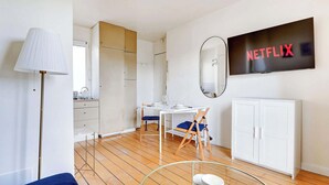 Une chambre moderne avec un plancher en bois, un bureau avec une chaise, une armoire, un téléviseur fixé au mur et une lampe.