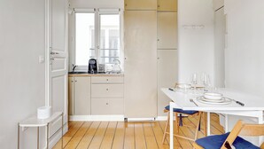 Une cuisine de taille réduite avec un coin repas, des meubles blancs et un plancher en bois.