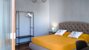 Une chambre d’hôtel moderne avec un grand lit, une tête de lit capitonnée, un luminaire suspendu et une petite table de chevet avec une lampe.