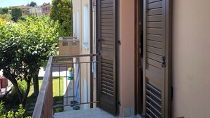 Un balcon avec un sol carrelé, un banc en bois et deux volets fermés.