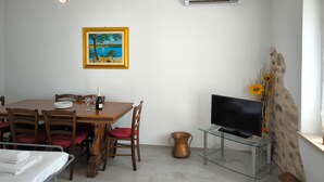 A dining area with a wooden table, chairs, a painting, a television on a glass stand, and a stone wall. - SG Family - Villa Secolo (Peschiera del Garda)