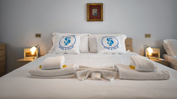 A hotel room with a neatly made bed, two pillows with the hotel's logo, bedside lamps, and a framed picture on the wall. - SG Family - Villa Secolo (Peschiera del Garda)