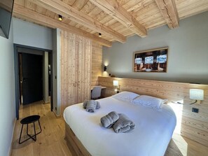 A bedroom with a large bed, wooden ceiling beams, a desk, and a chair.
