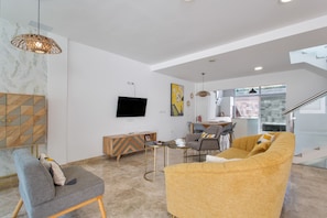 A modern living room with a sofa, armchair, TV, and dining area.