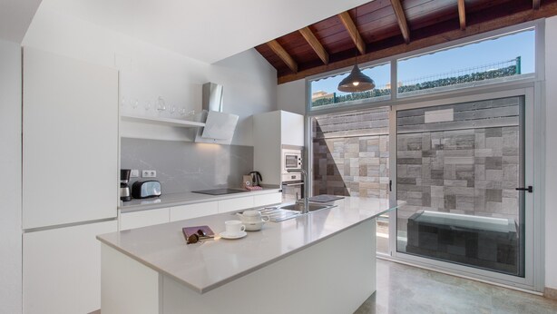 A modern kitchen with a large island, built-in appliances, and a view through a glass door.