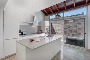 A modern kitchen with a large island, built-in appliances, and a view through a glass door.