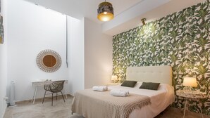 A bedroom with a bed, a desk, a chair, a round mirror, and a wall with a leafy pattern.