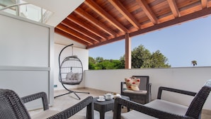 A covered outdoor seating area with wicker furniture, a hanging chair, and a table with a teapot.