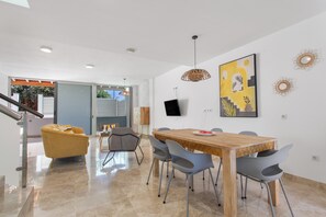 A modern dining area with a wooden table, grey chairs, a yellow armchair, and a TV mounted on the wall.