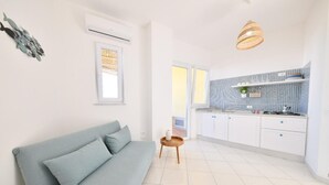 Ett modernt vardagsrum med en ljusblå soffa, ett litet träbord och en köksdel med vita skåp och ett mönstrat stänkskydd.