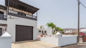 A two-story building with a dark garage door, a balcony with railings, and a clear sky. - 'Elikasa Mala' Holiday Apartment with Sea View, Balcony and Wi-Fi (Mala)