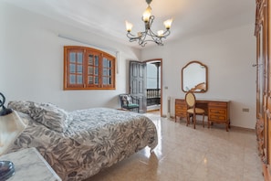 Une chambre à coucher comprenant un lit, une commode, un miroir, un lustre et donnant sur l’extérieur.