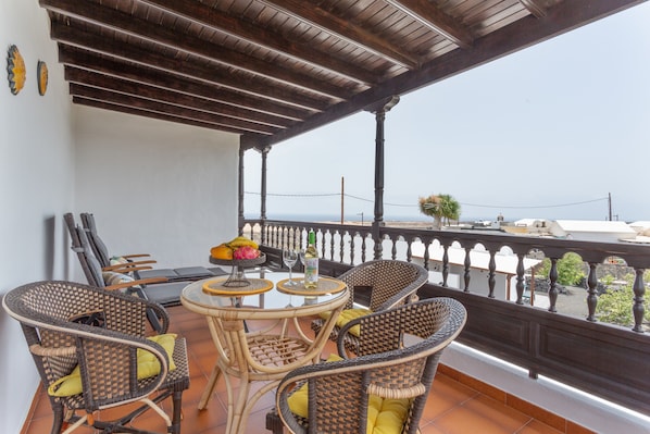 Un balcon agrémenté de meubles en osier, une table avec un panier de fruits et une vue sur la mer.