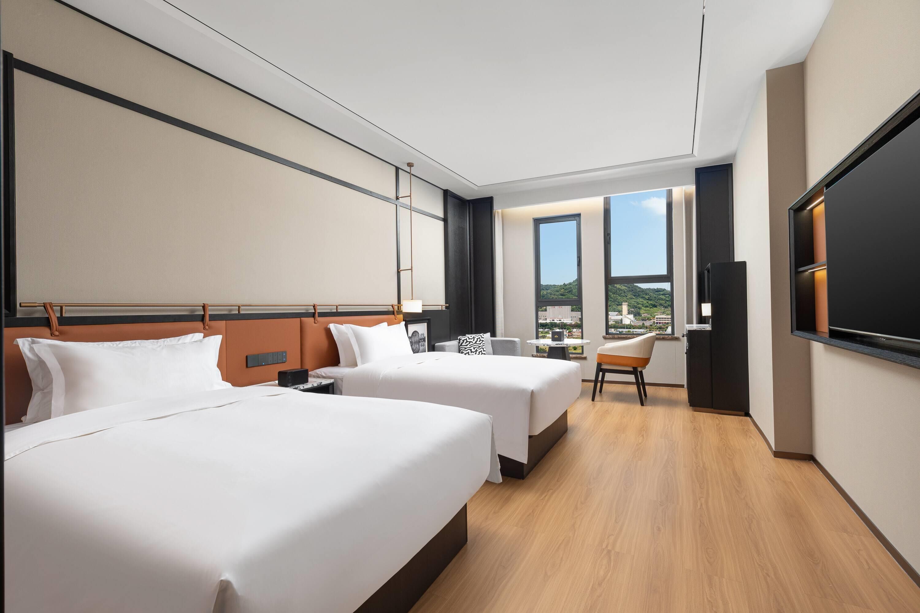 Une chambre d’hôtel avec deux lits, un bureau, une chaise, une télévision et une grande fenêtre donnant sur la ville.