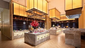 A modern hotel lobby with a central reception desk, multiple seating areas, and a decorative plant arrangement.