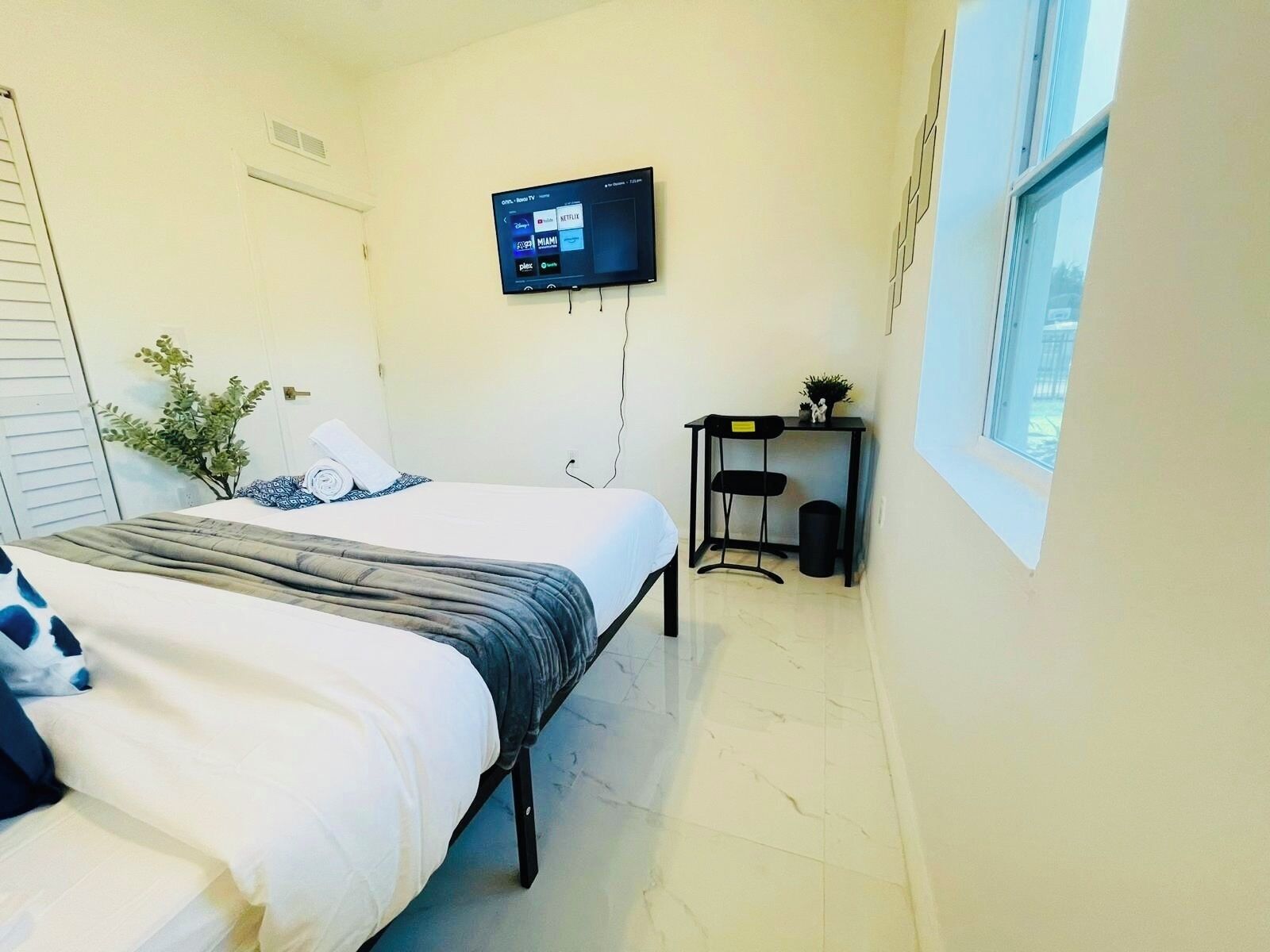 A hotel room with a bed, a desk, a TV mounted on the wall, and a window.