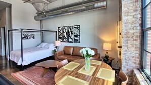 Una habitación de hotel con cama con dosel, un sofá de cuero marrón, una mesa redonda de madera y un jarrón con flores blancas.